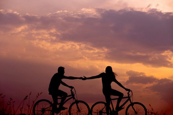 Verbindung zwei Menschen reichen sich auf dem Fahrrad bei Sonnenuntergang die Hand
